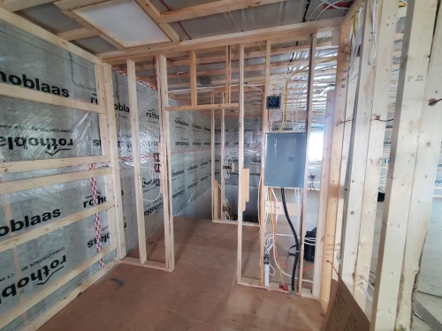 Wood stud wall prior to being covered by drywall; containing electrical wiring, outlets and electrical panel